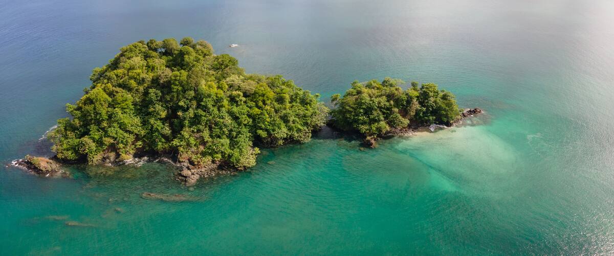 An aerial view of two lush, forested islands surrounded by turquoise waters.