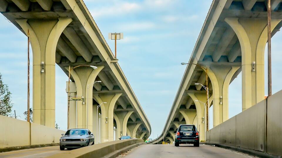 A multi-lane highway with a concrete barrier on one side and a bridge with a series of arches on the other.