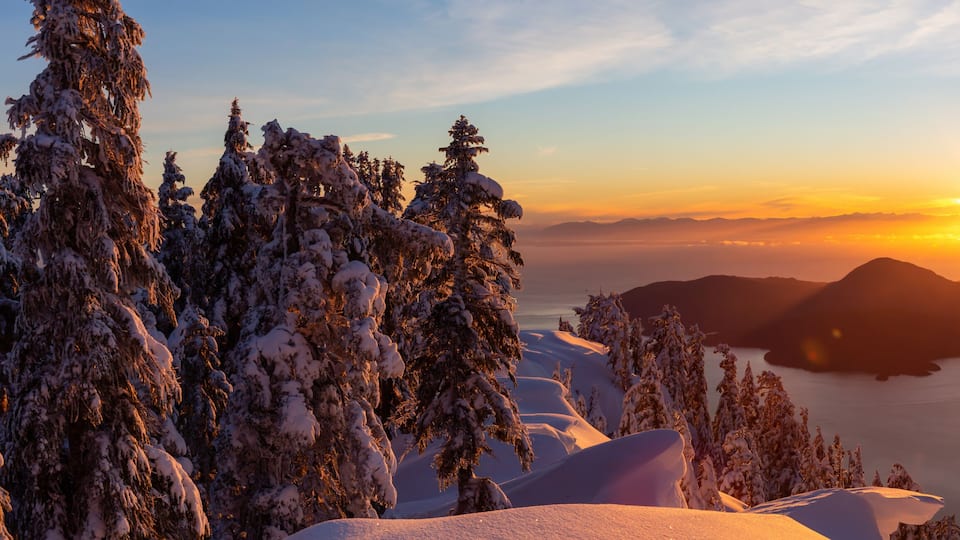 A sunset over a snow-covered landscape with mountains and a body of water.