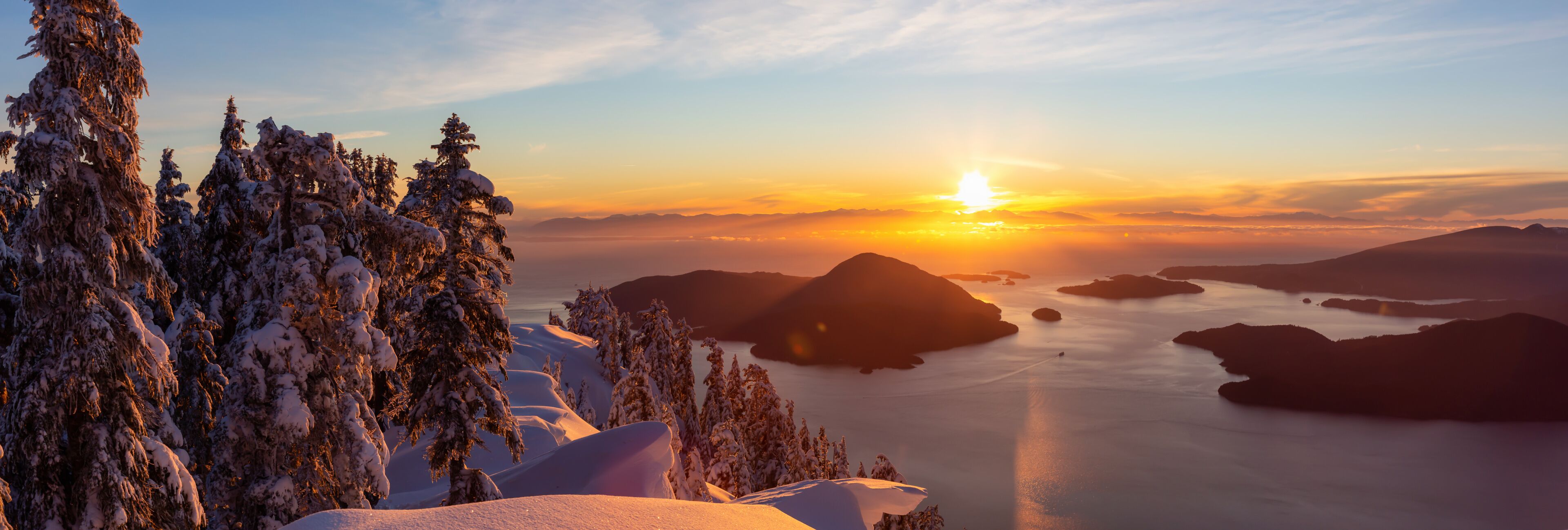 A sunset over a snow-covered landscape with mountains and a body of water.