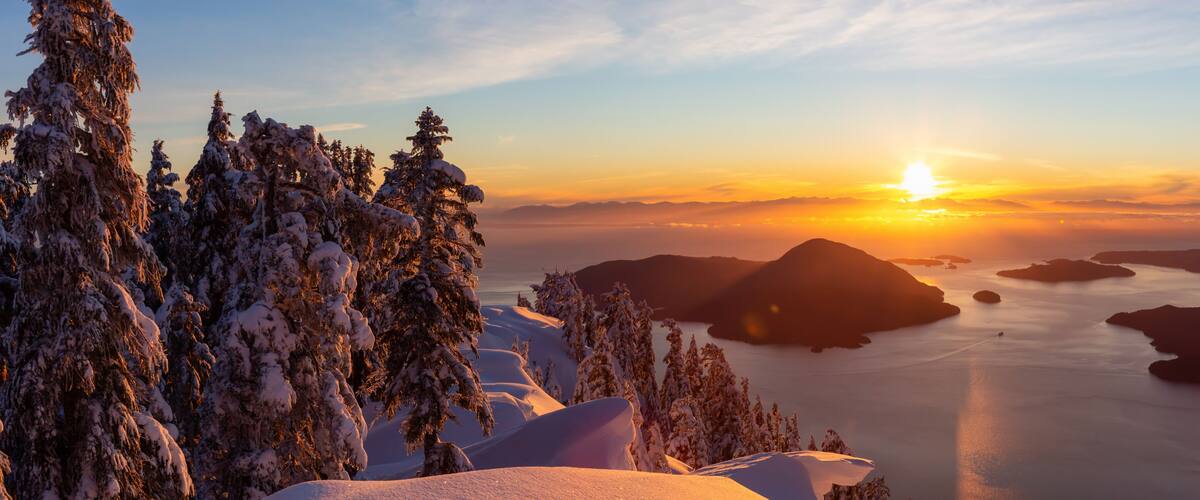 A sunset over a snow-covered landscape with mountains and a body of water.