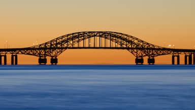 Slow release view of the Robert Moses Causeway bridge in Babylon, NY against an orange sunrise. The long exposure smooths the water and gives it a beautiful blue color