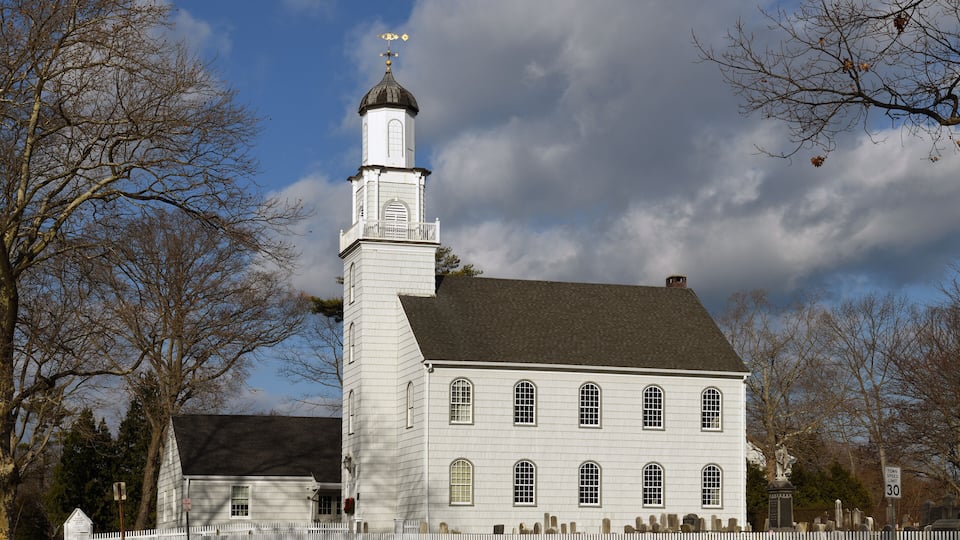 A white church with a steeple and a white picket fence.