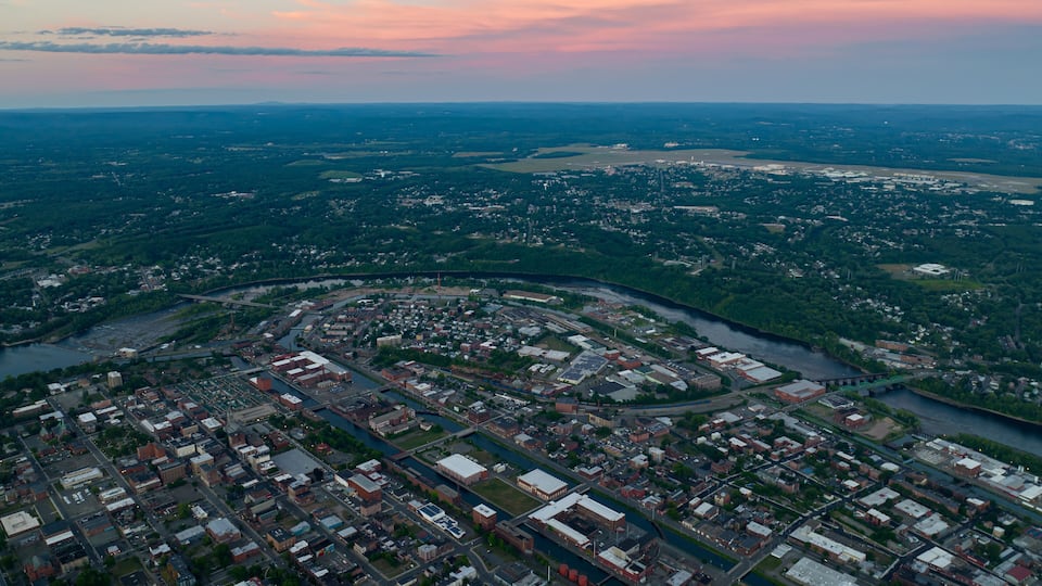 An aerial view of a city with a river running through it, surrounded by green areas.