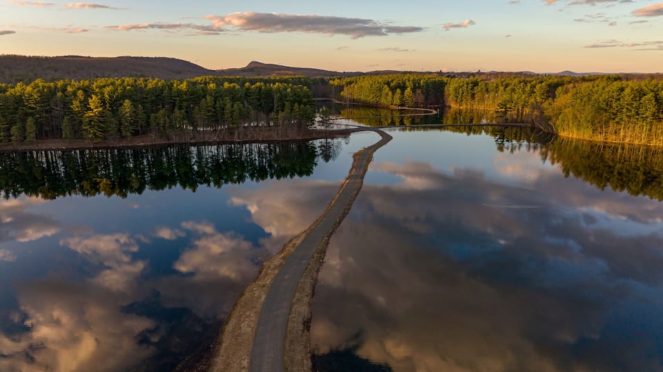 A forested landscape with a winding road leading to a body of water, surrounded by hills.