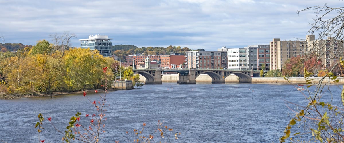A river with a bridge, autumn trees, and buildings in the background.