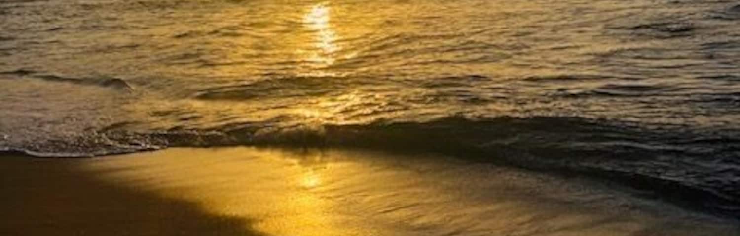 A sunset over a beach with waves gently lapping the shore.