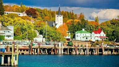 A waterfront town with a church, docked boats, and colorful autumn trees.