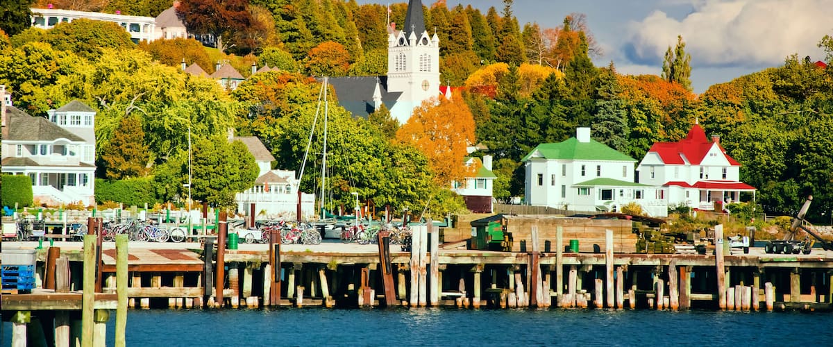 A waterfront town with a church, docked boats, and colorful autumn trees.