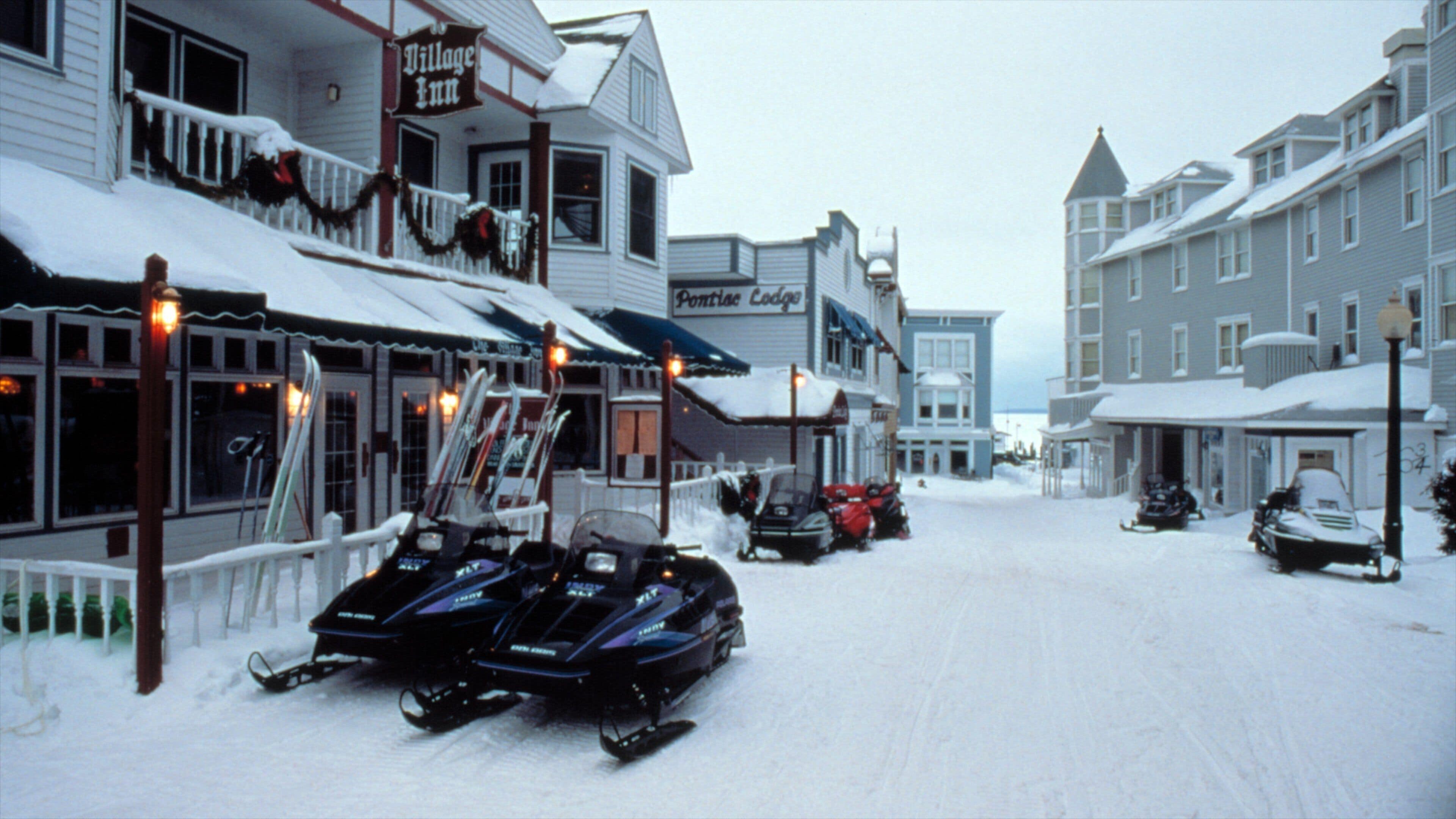 Una calle nevada con edificios, incluyendo un Village Inn y un Pontiac Lodge.
