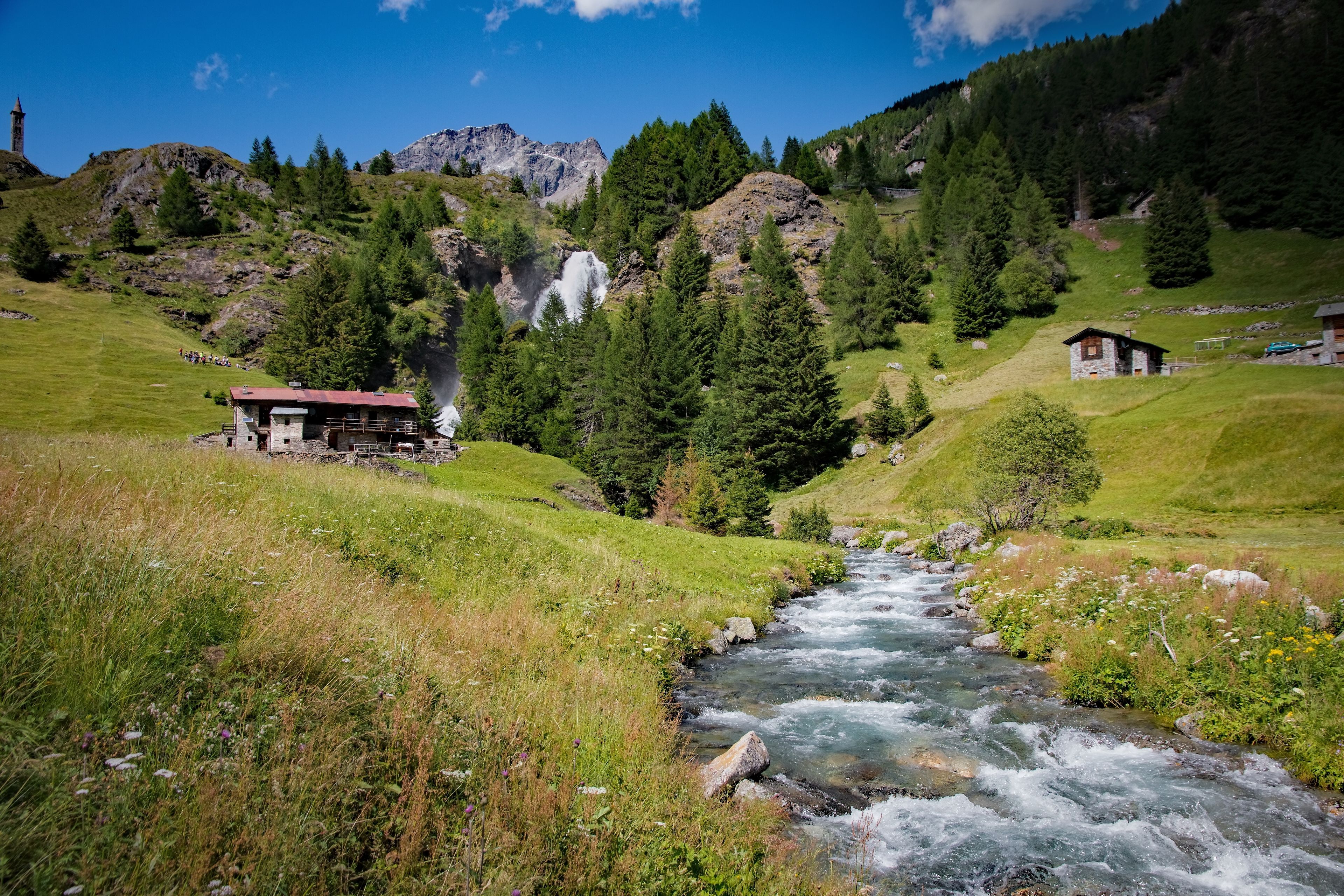 Un paysage de montagne avec une rivière sinueuse, un petit chalet et une tour.