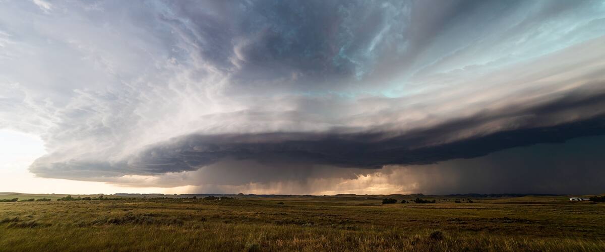 A stormy sky over a grassy field with a distant house.