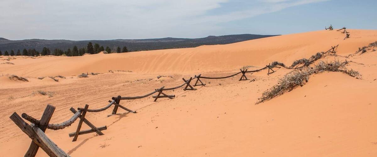 A desert landscape with sand dunes and a wooden fence.