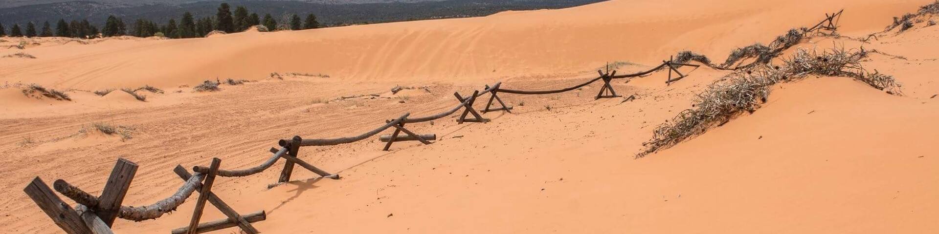A desert landscape with sand dunes and a wooden fence.