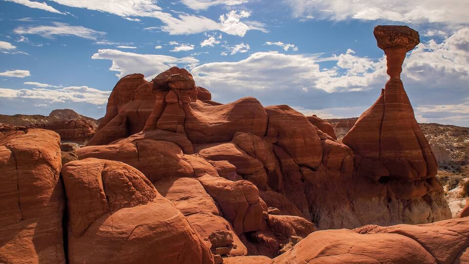 A desert landscape with prominent red rock formations and a clear blue sky with scattered clouds.