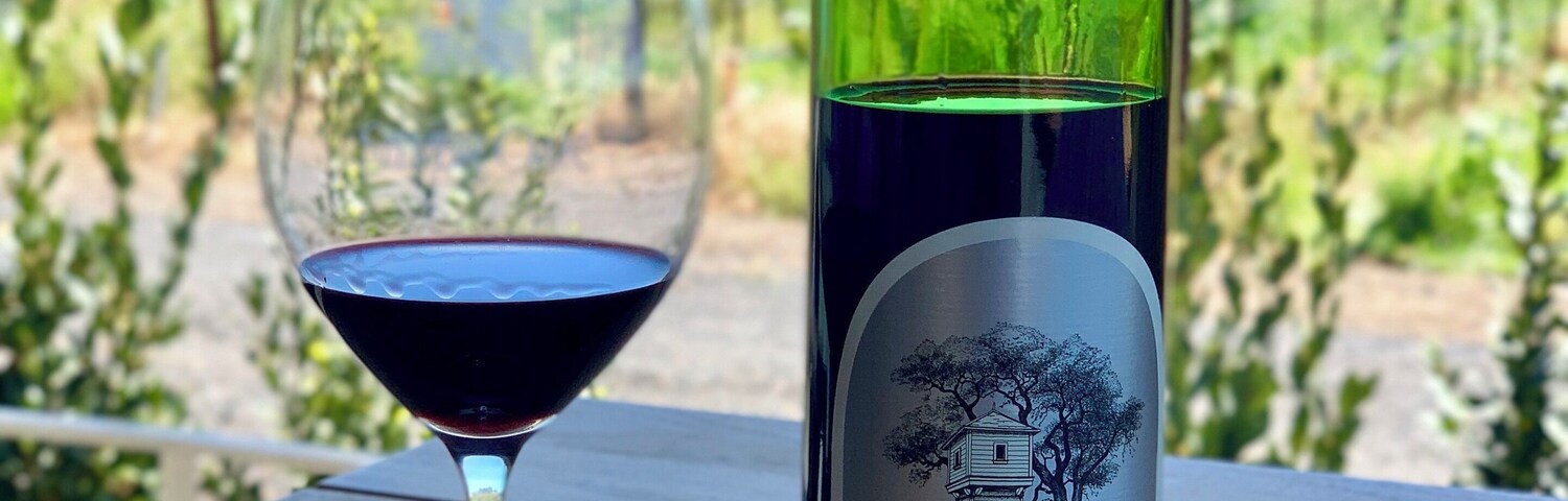 Eine Flasche Silver Oak Wein und ein Glas Rotwein auf einem Holztisch, im Hintergrund ein Weinberg.