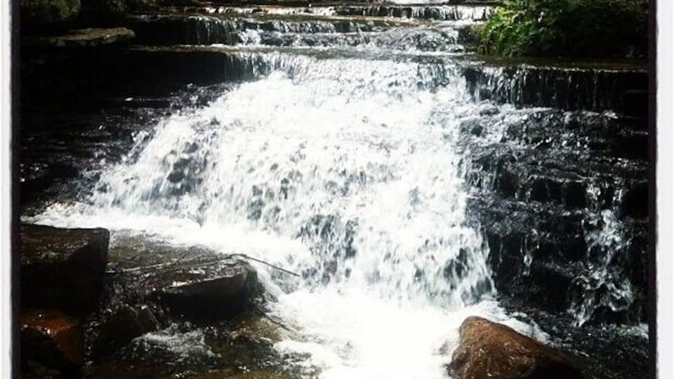A multi-tiered waterfall surrounded by rocks and greenery.
