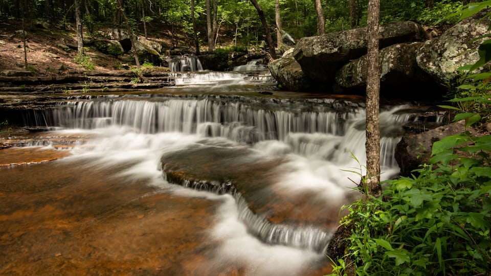 A waterfall in a forested area with rocky terrain and lush greenery.