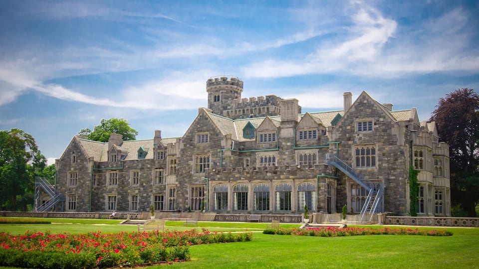 A large stone building with a tower, surrounded by a well-maintained lawn and flower beds.