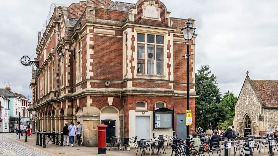 A historic building with a clock, a red post box, and outdoor seating.