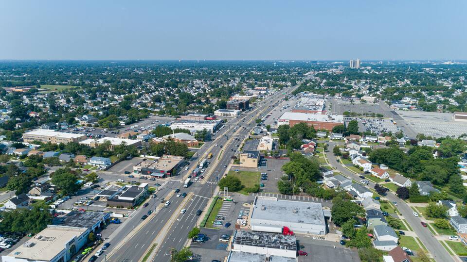 An aerial view of a city with a wide road, residential areas, and commercial buildings.