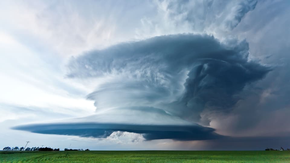 A vast green field under a dramatic sky with a large, dark cloud formation.
