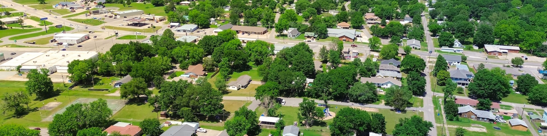 Aerial view suburbs of Checotah, McIntosh County, Oklahoma toward north of interstate I-40, east of Highway 69, suburban single-family houses on large lot size lush trees along 4th street, sunny