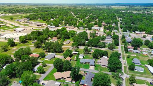 Aerial view suburbs of Checotah, McIntosh County, Oklahoma toward north of interstate I-40, east of Highway 69, suburban single-family houses on large lot size lush trees along 4th street, sunny