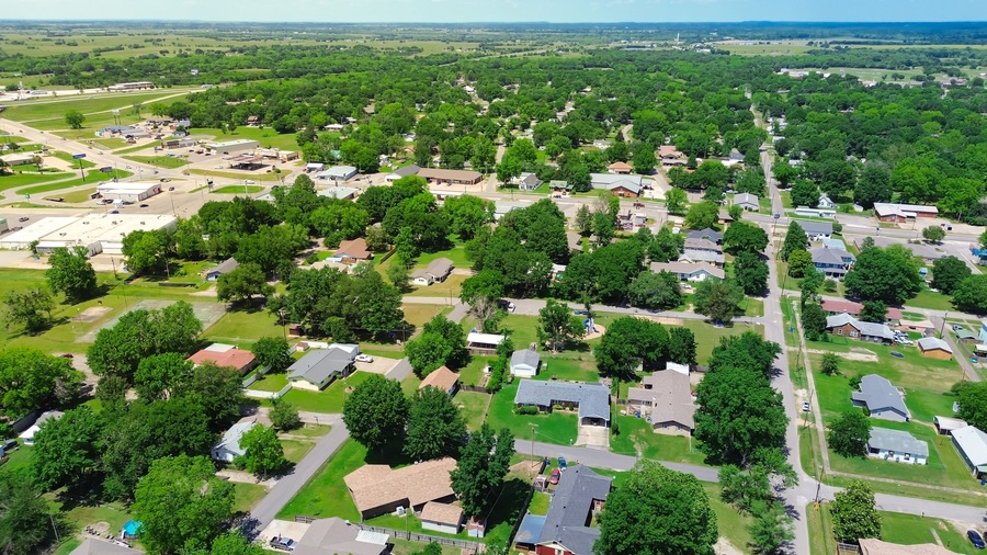 Aerial view suburbs of Checotah, McIntosh County, Oklahoma toward north of interstate I-40, east of Highway 69, suburban single-family houses on large lot size lush trees along 4th street, sunny