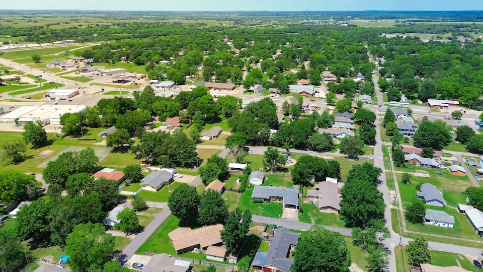 An aerial view of a suburban area with houses, roads, and green spaces.