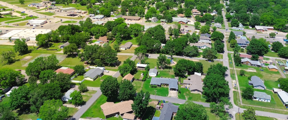 An aerial view of a suburban area with houses, roads, and green spaces.
