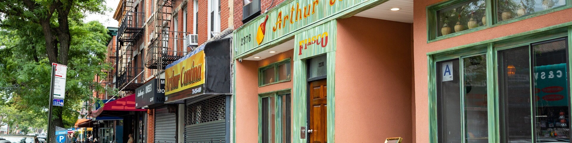 A street with Arthur Avenue storefronts, including Arthur's Candies and Fiasco.