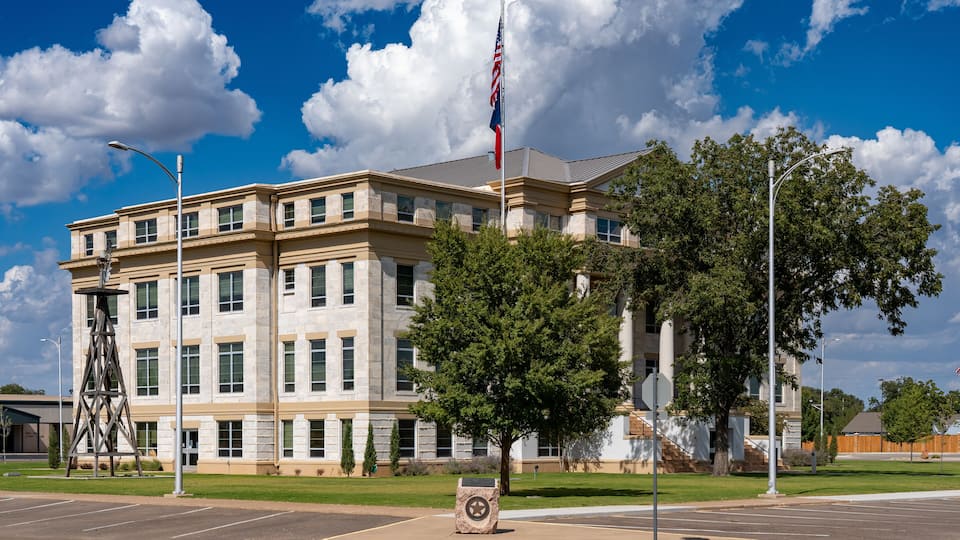 A building with a flagpole, a tree, and a parking lot.