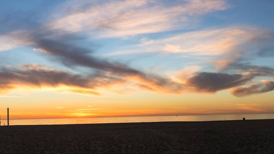 A beach at sunset with a lifeguard tower and a clear sky with clouds.