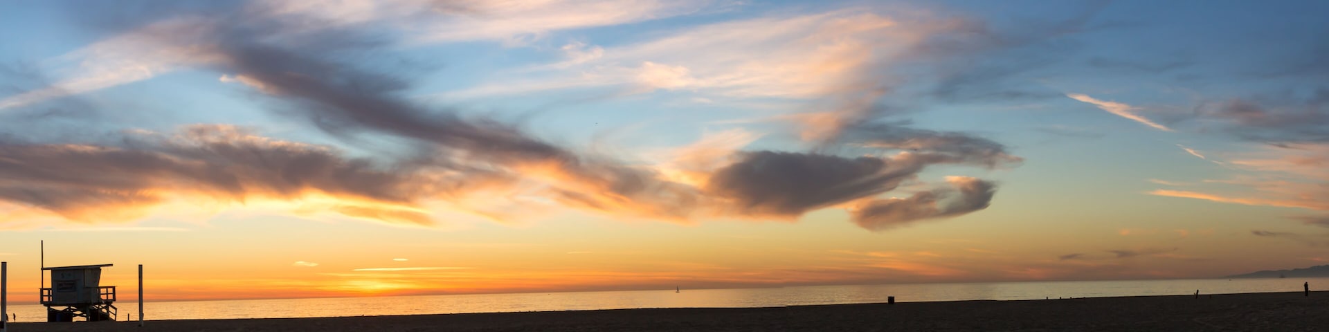 Una playa al atardecer con una torre de salvavidas y un cielo despejado con nubes.
