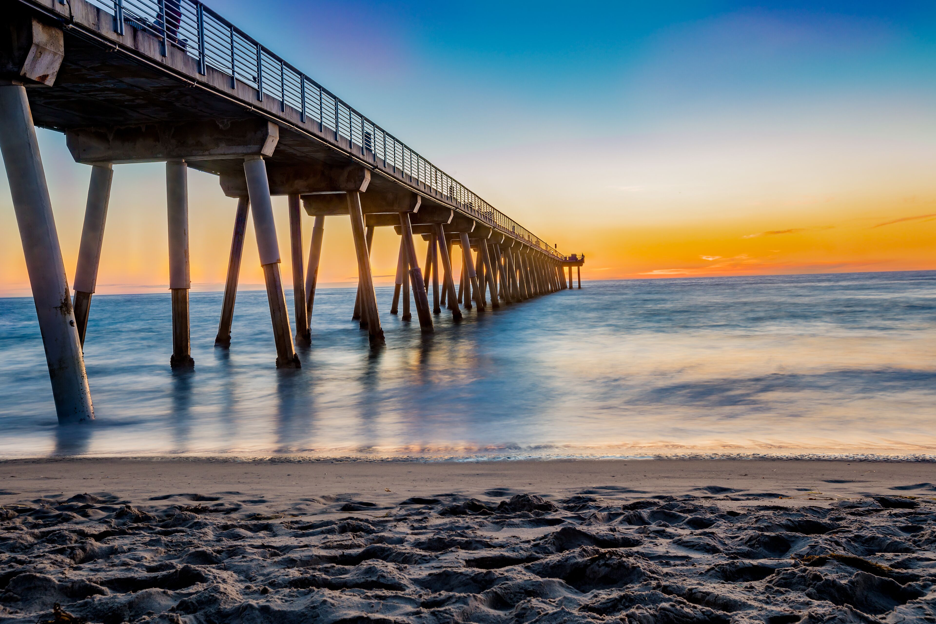 A pier extending into calm waters at sunset with a clear sky.