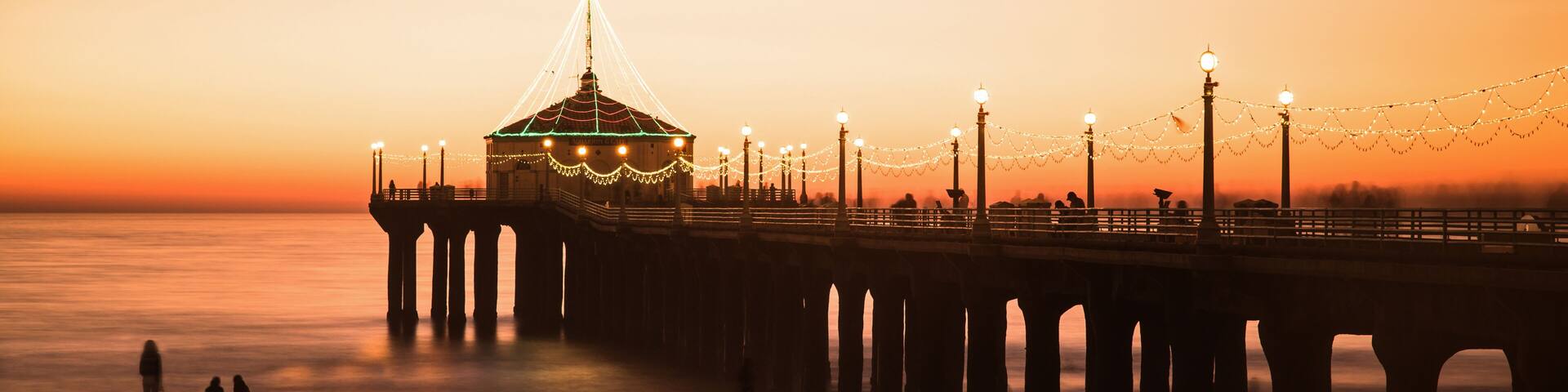 A pier with a dome structure, string lights, and a sunset over the water.