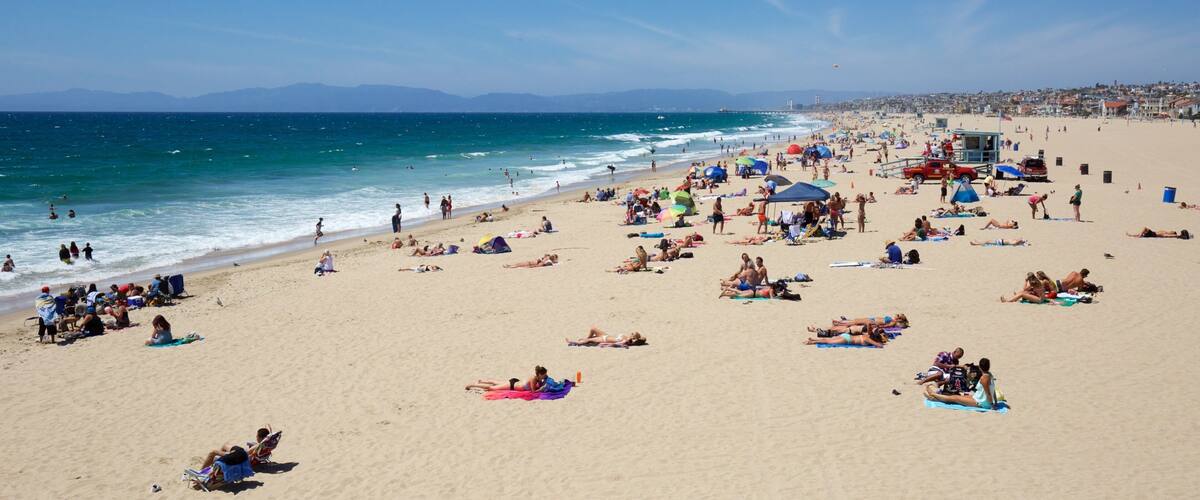 Une plage bondée où les gens se prélassent au soleil et se baignent.