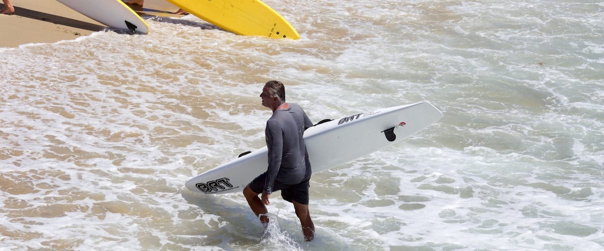 A man carrying a surfboard walking through the water.