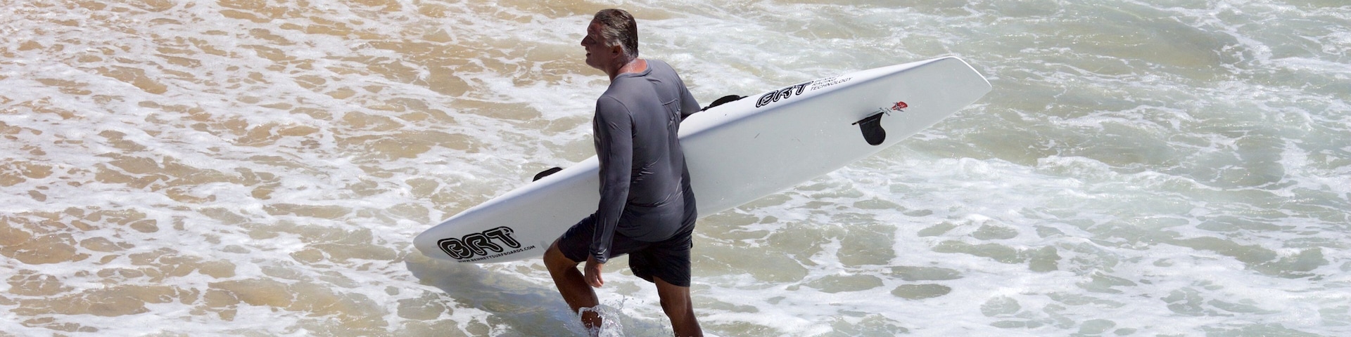 A man carrying a surfboard walking through the water.
