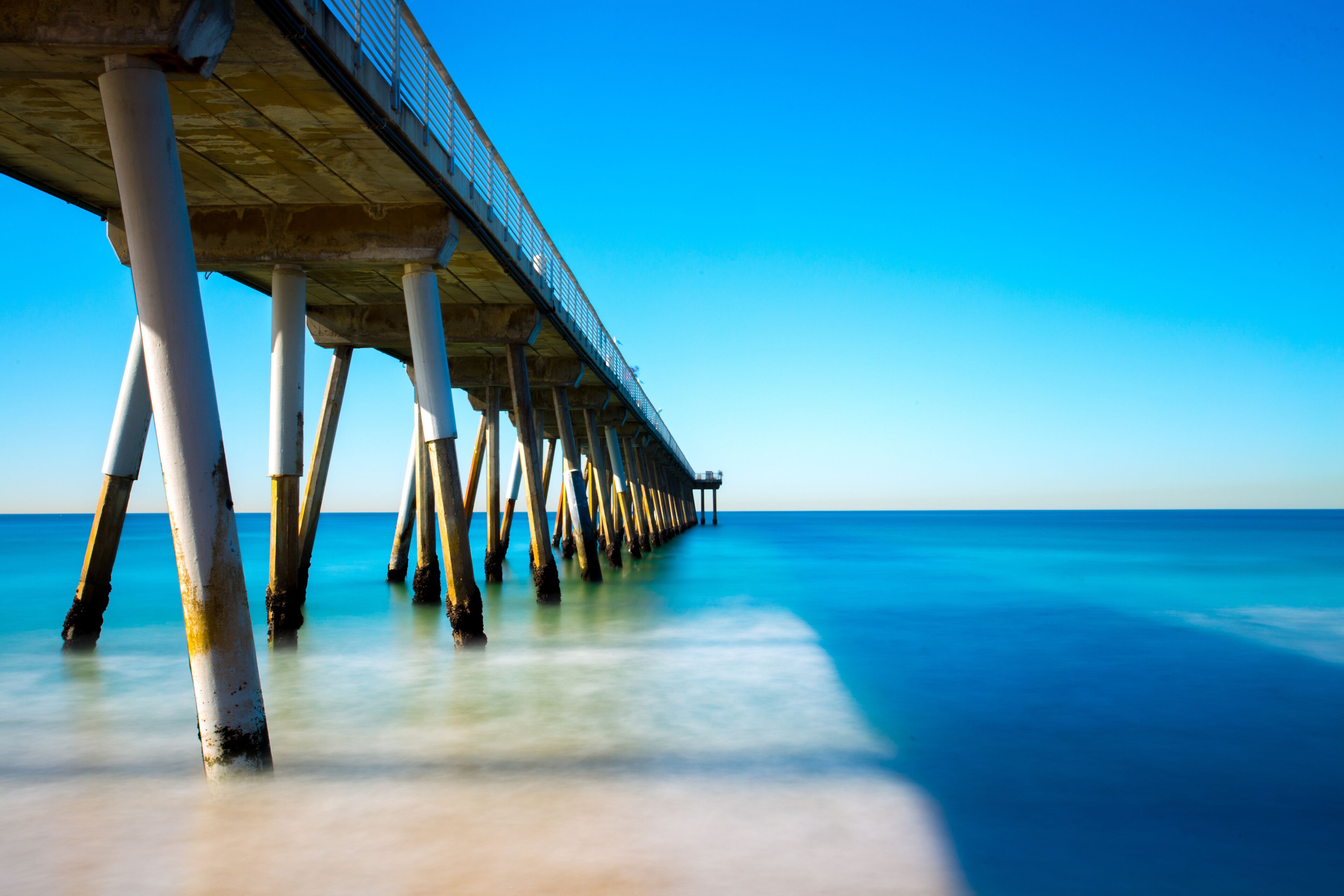 A pier extending into the ocean with clear blue water and a bright sky.
