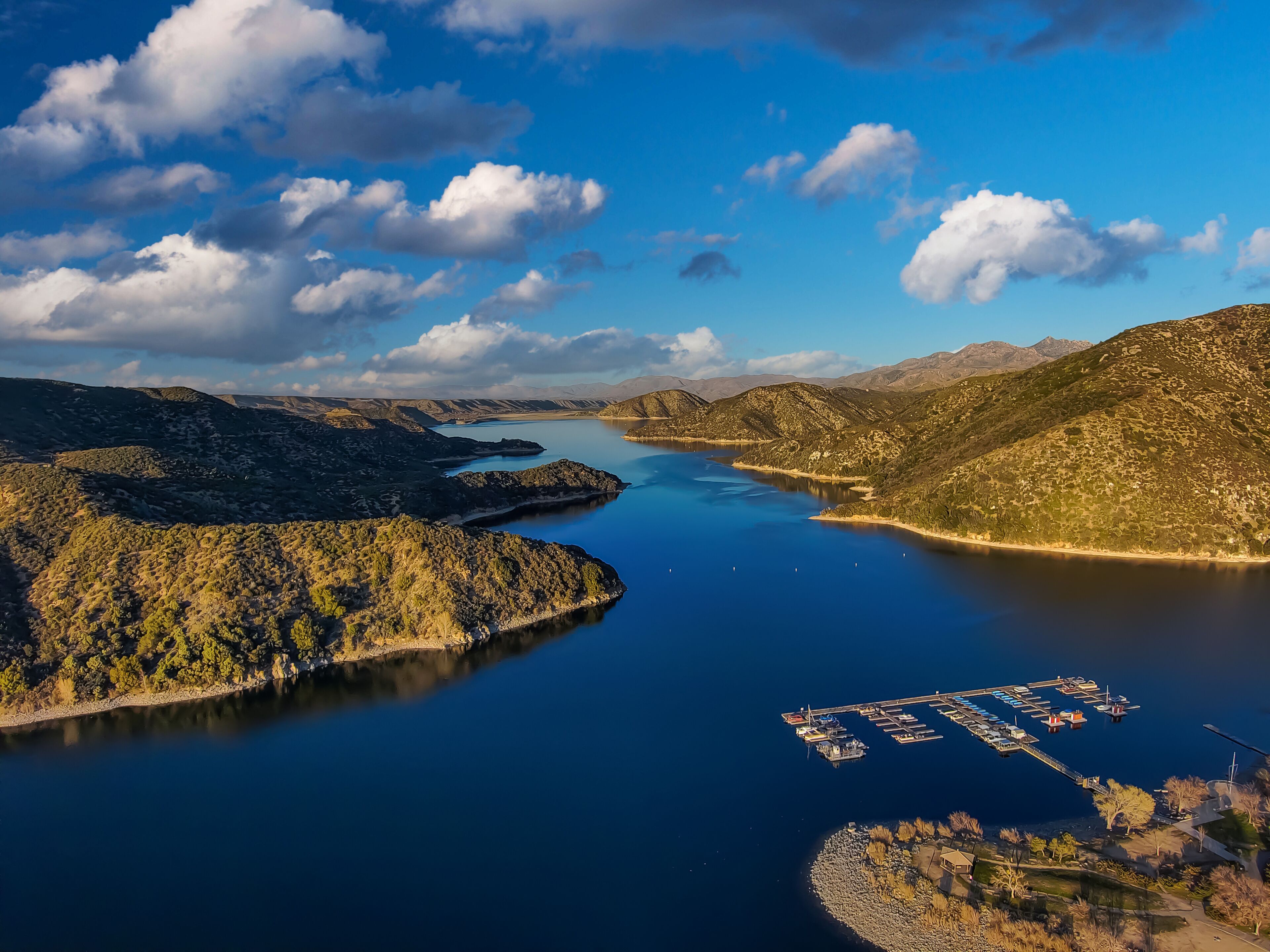 a gorgeous shot of the vast blue lake surrounded by majestic mountain ranges with a boat dock, blue sky and clouds at Silverwood Lake in Hesperia California USA