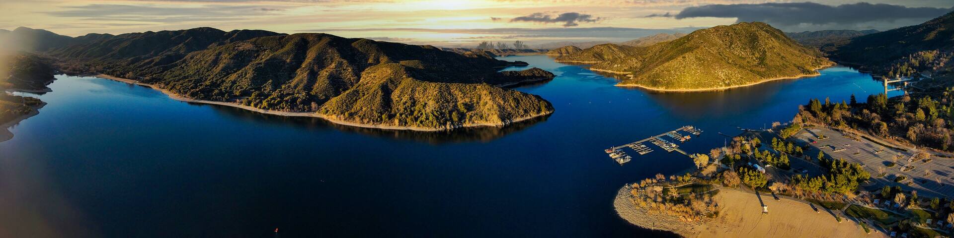 a majestic aerial panoramic shot of the vast blue still lake water with breathtaking mountain ranges reflecting off the lake with powerful clouds at sunset at Silverwood Lake in Hesperia California