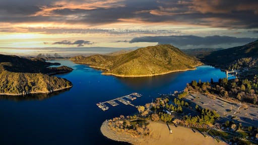 a majestic aerial panoramic shot of the vast blue still lake water with breathtaking mountain ranges reflecting off the lake with powerful clouds at sunset at Silverwood Lake in Hesperia California