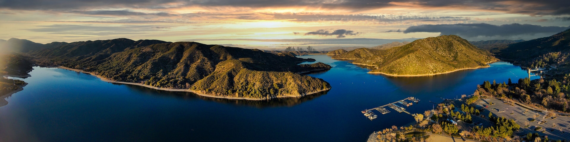 a majestic aerial panoramic shot of the vast blue still lake water with breathtaking mountain ranges reflecting off the lake with powerful clouds at sunset at Silverwood Lake in Hesperia California