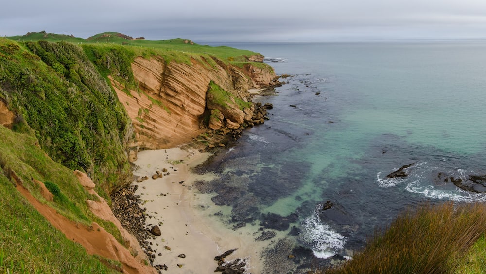 Elevated view of red sandstone cliffs and a small beach on the Chatham Islands, New Zealand.