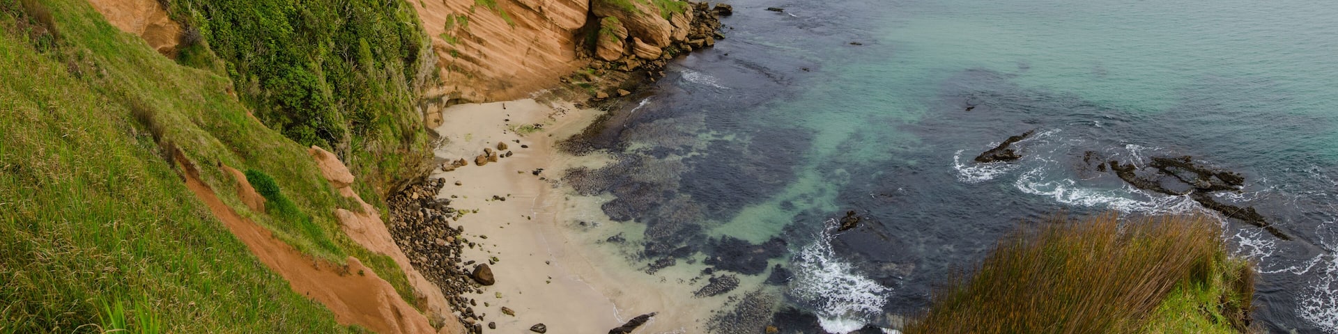 Elevated view of red sandstone cliffs and a small beach on the Chatham Islands, New Zealand.