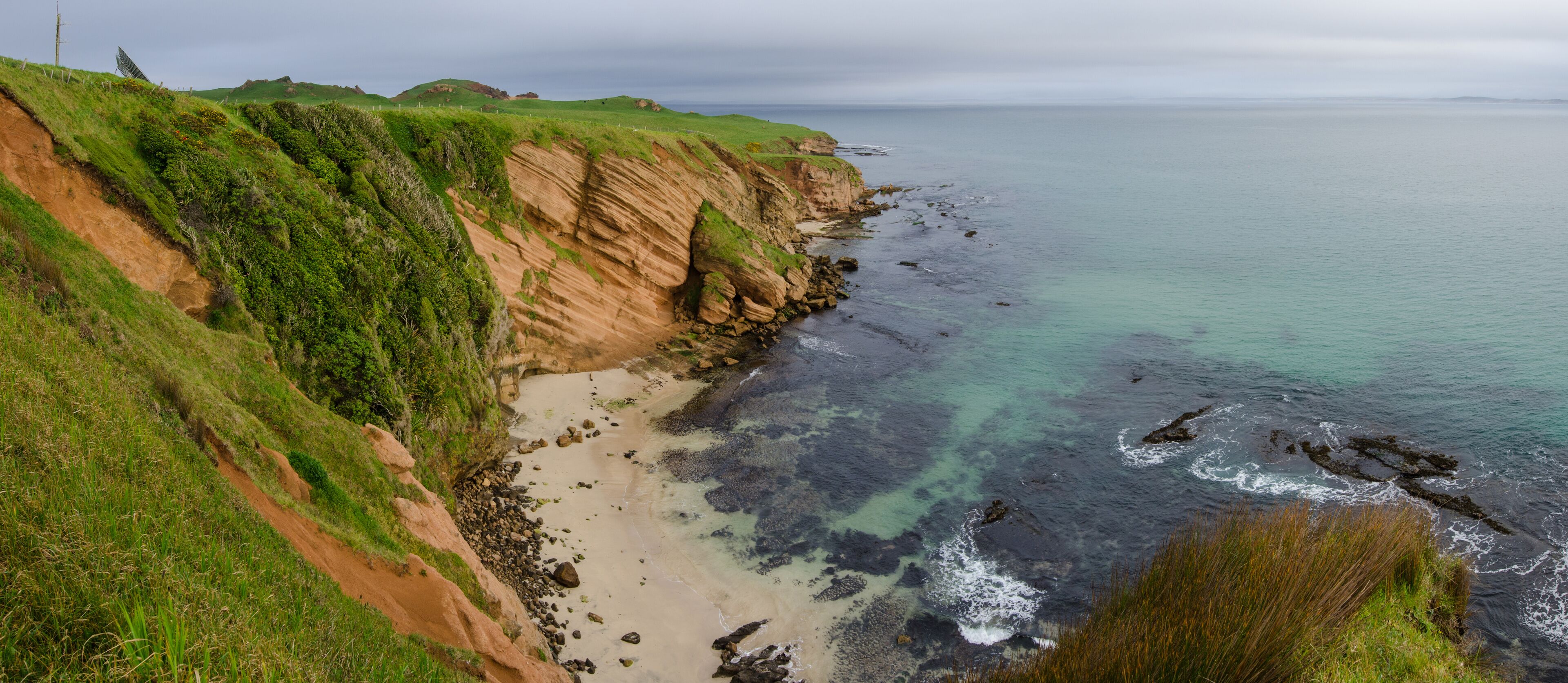 A coastal landscape with a sandy beach, rocky cliffs, and green vegetation.