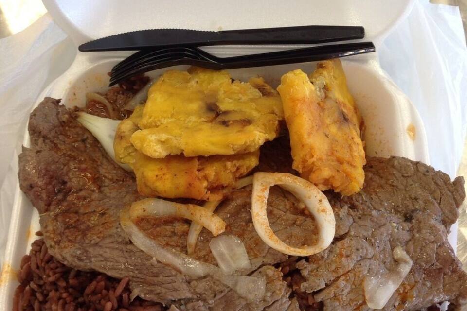 Afhaalmaaltijd met rijst, rundvlees, gebakken plantains en uien in een piepschuim bak.