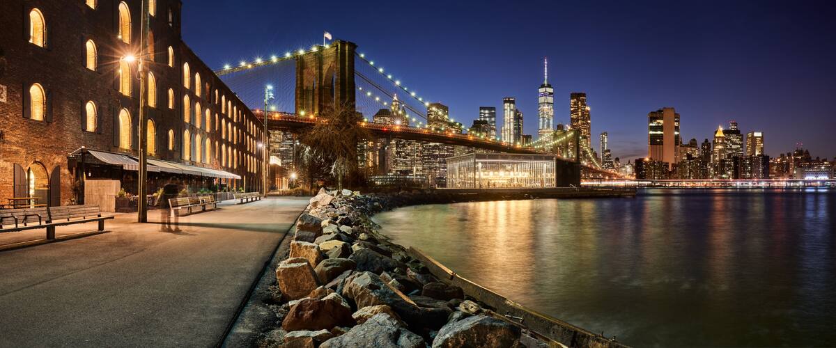 A nighttime cityscape with a prominent bridge, a river, and a historic building with arched windows.